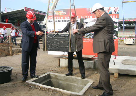 Berlins Innen- und Sportsenator Frank Henkel, Architekt Dirk Thieme und Klubpräsident Dirk Zingler lassen eine Truhe mit zeitgemäßen Erinnerungsstücken in den Boden unter den Tribüne-Grundstein.